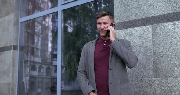 Serious Man Tries to Call Then Takes Off and Puts Phone Into a Pocket Outdoors