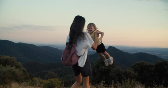 Cheerful Woman Holding Daughter on Hands and Spin Around on Epic Mountain View