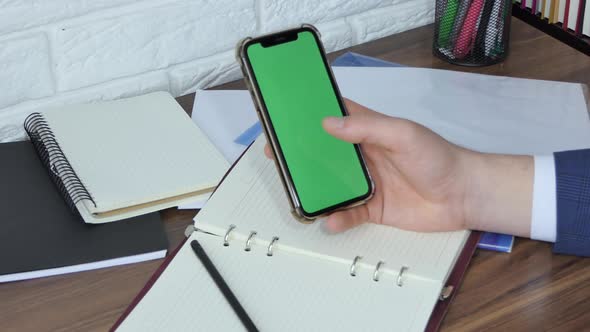 Man Using Smart Phone in Office Space Sitting on Chair and Using Green Screen Phone Mockup Chroma