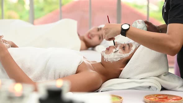 Beautiful Asian woman enjoying applying white mud to her face. at a luxury spa resort