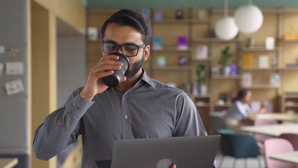 Happy Indian Businessman Holding Coffee and Laptop Walking in Office