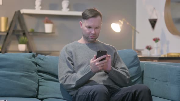 Casual Man Using Smartphone While Sitting on Sofa