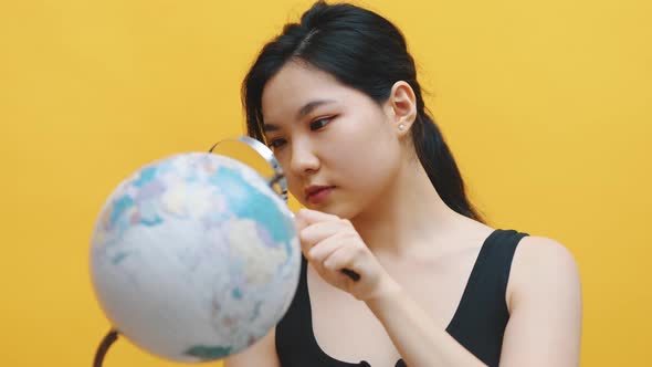 Young Asian Woman Examining the Globe with a Magnifying Glass