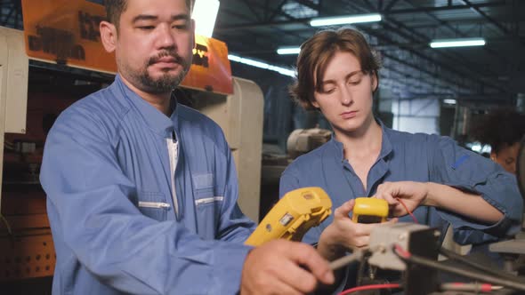 Two professional engineers inspect machines' electric systems at the factory.