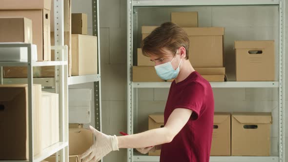 Man Employee of Warehouse Wearing Medical Mask and Gloves Taking Photo of Parcel Using Smartphone