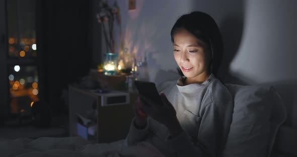 Woman using cellphone on bed at night