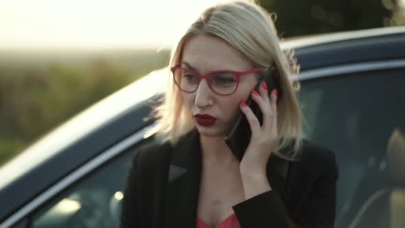 The Blonde Talking on the Phone Emotionally at Car on Highway at Sunset