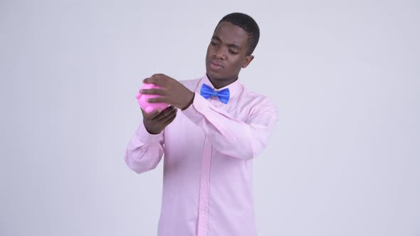 Young Sad African Businessman Holding Piggy Bank and Giving Thumbs Down