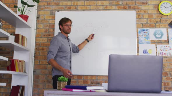 Caucasian male teacher teaching chemistry while looking at laptop in the classroom at school