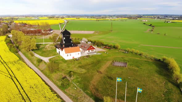 Drone circling windmill from far flying over rapsmark. Sweden springtime