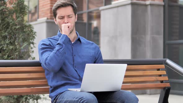 Sitting Outdoor Young Man Coughing While Working on Laptop