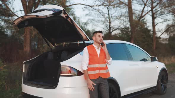 Man With Reflective Vest Calling by Phone About Breakdown in Her Electric Car. Emergency Stop Sign