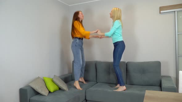 women with light and dark hair jump together on large sofa in the living room.