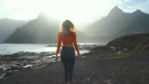 A Woman Walks Next to the Ocean and Raises Her Hands Up and Enjoying the Moment on Volcanic Beach of