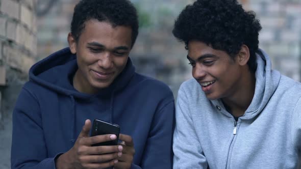 Black male teenager showing friend photos on smartphone