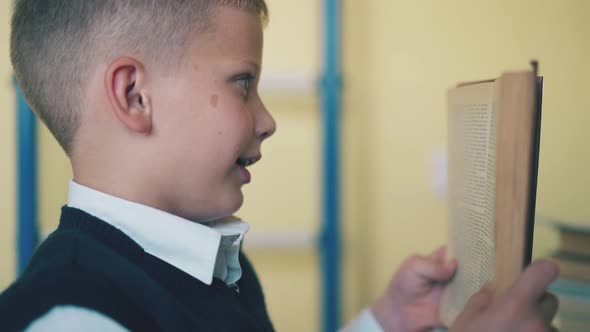 Kid Turns Page of Textbook in Room on Blurred Background