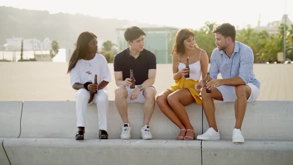 Multiracial Young Women and Men with Beer Laughing and Talking on Summer Evening at Seafront