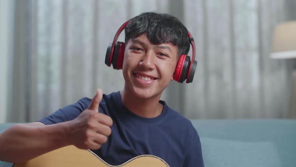 Boy Composer With Headphones Smiling And Showing Thumbs Up Gesture To Camera While Playing Guitar