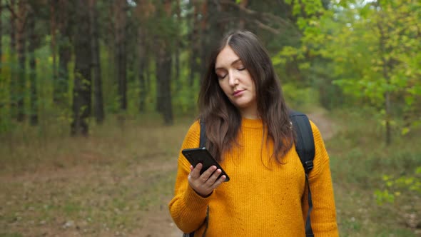 Pretty Tourist Looks at Cellphone Screen in Green Forest