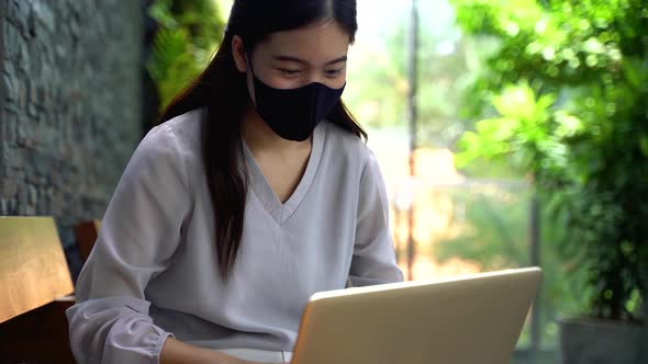 Asian Woman Wearing a Face Mask Outside While Sitting on Laptop