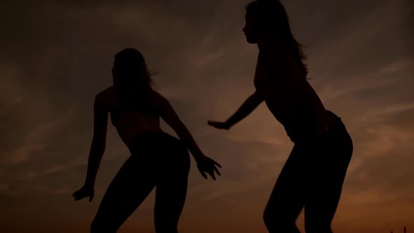 Silhouettes of Two Beautiful Girls Dancing Zumba in Field at Sunrise