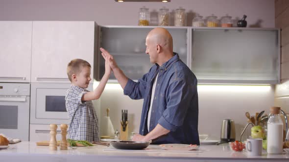 Father and Son High-Fiving while Cooking Breakfast in Kitchen