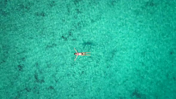 Zoom out aerial view of pregnant woman floating on her back in transparent sea.