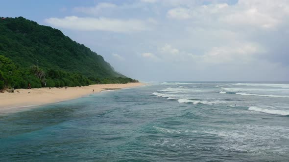 coastline beach with ocean waves crash on island with tall mountains, aerial