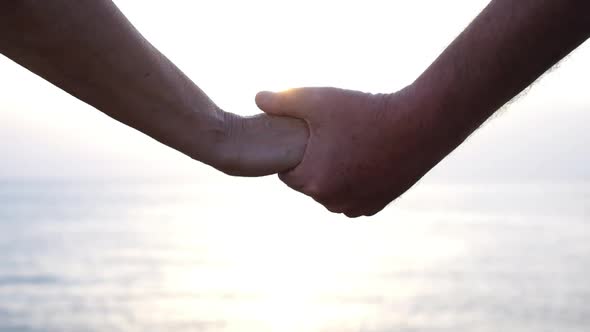 close up and portrait of hands taking care with each other with sunset and sea or ocean