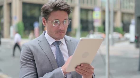 Middle Aged Businessman Browsing Internet on Tablet Outdoor