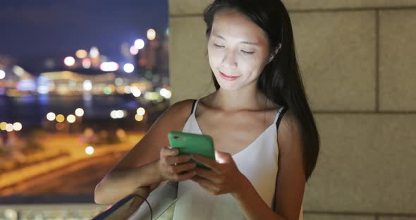 Woman looking at mobile phone with the background of cityscape in Hong Kong 