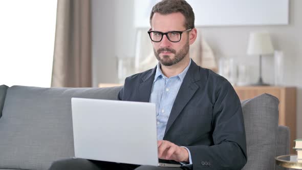 Young Businessman with Laptop Pointing with Finger at Home