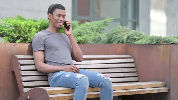 Young African Man Talking on Smartphone on Bench