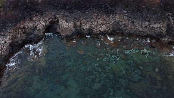 Top down birds eye view aerial shot of a rocky coastline with calm sea water