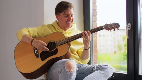 Young Man Playing Guitar Sitting on Windowsill