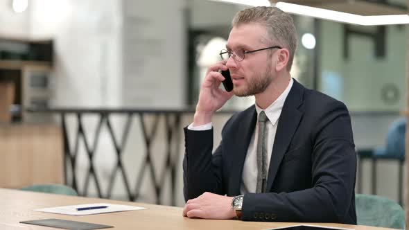 Cheerful Young Businessman Talking on Smartphone in Office