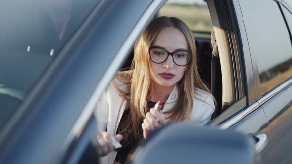 Business Lady Looking in Rear View Mirror and Applying Red Lipstick in Car