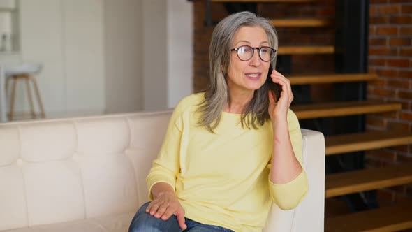 Cheerful Grayhaired Woman Glad to Talking on Smartphone Sitting on the Sofa at Home