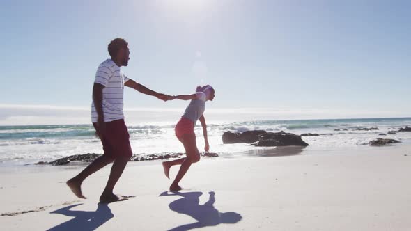 African american couple holding hands and running on the beach