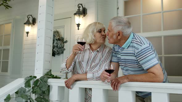 Senior Elderly Caucasian Couple Drinking Wine, Looking Ahead, Making a Kiss in Porch at Home