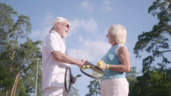 Positive Smiling Mature Couple After Playing Tennis on the Tennis Court Shaking Hands