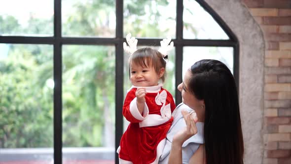 Young Beautiful Mum Holding Her Caucasian Child in Santa Clause and Waving at Each Other at Home