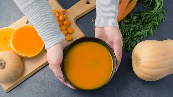 Hands Putting Bowl of Pumpkin Cream Soup on Table 
