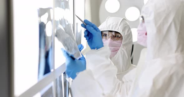 Two Doctors in Protective Suits and Masks Looking at Xrays