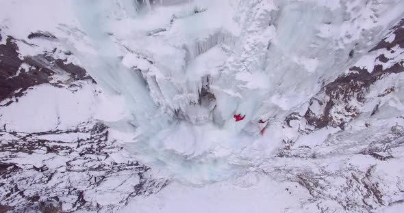 Aerial drone view of a man ice climbing on a frozen waterfall in the mountains.