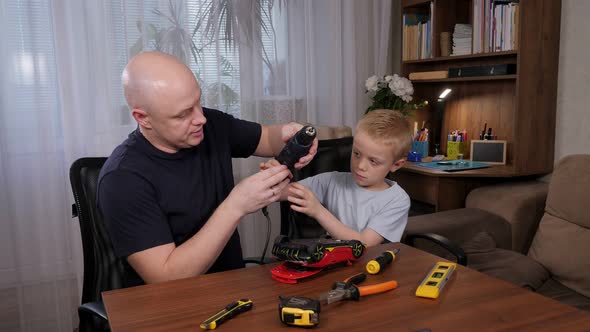 A Man and a Little Boy are Sitting at a Table and Repairing a Broken Toy Car