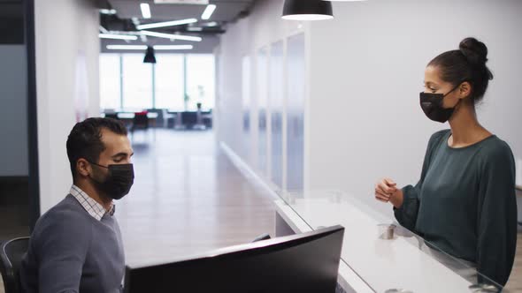 Mixed race woman in face mask has temperature checked by male colleague at office reception desk