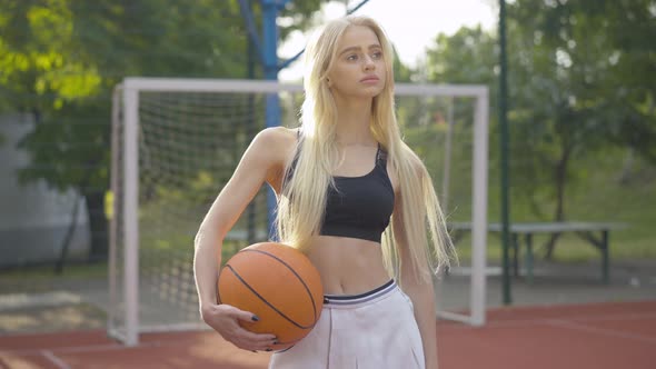 Portrait of Charming Thoughtful Young Woman Standing with Ball in Sunlight. Camera Approaches To