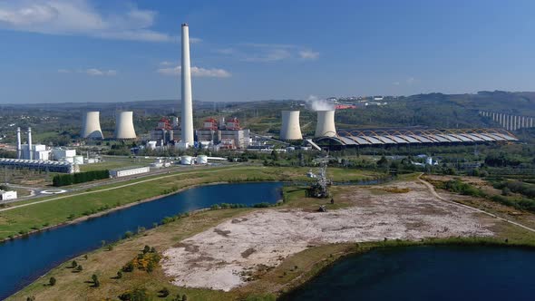 Thermal power plant with smoking chimney behind the lake and an old drill, bridge on the right, brig