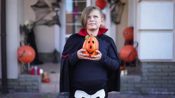 Happy Confident Caucasian Boy in Halloween Vampire Costume Standing with Jack O'Lantern Outdoors